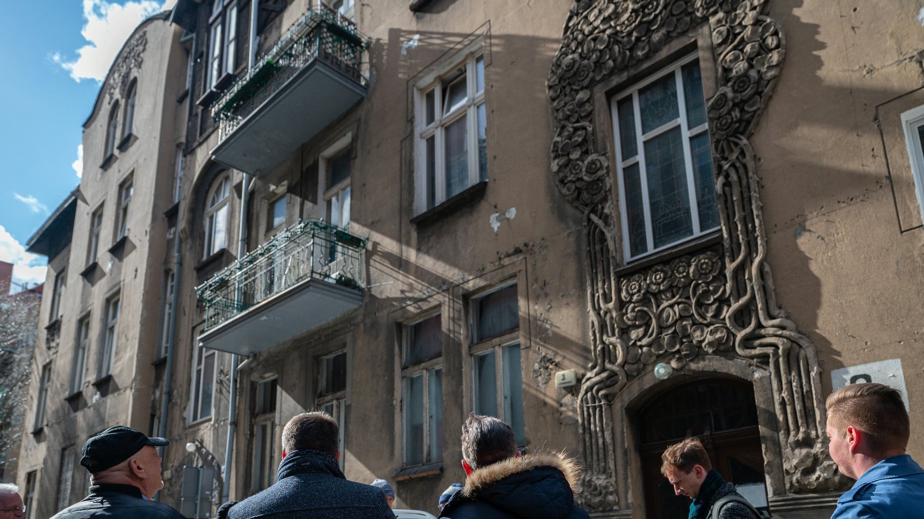 Na zdjeciu grupa osób przed secesyjną kamienicą