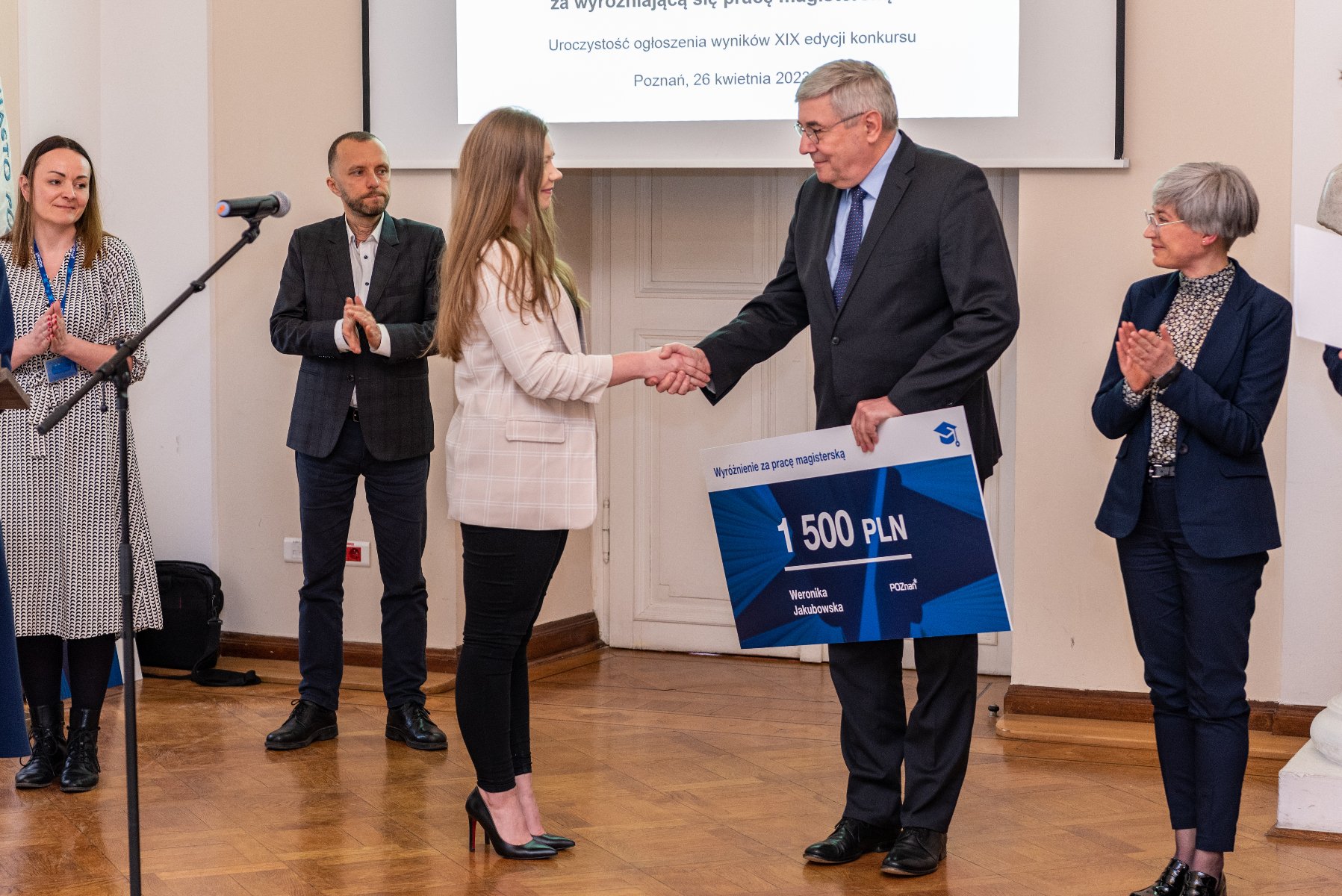 Na zdjęciu przedwodniczący rady miasta wręcza czek jednej z laureatek, w tle stoi trójka ludzi - grafika artykułu