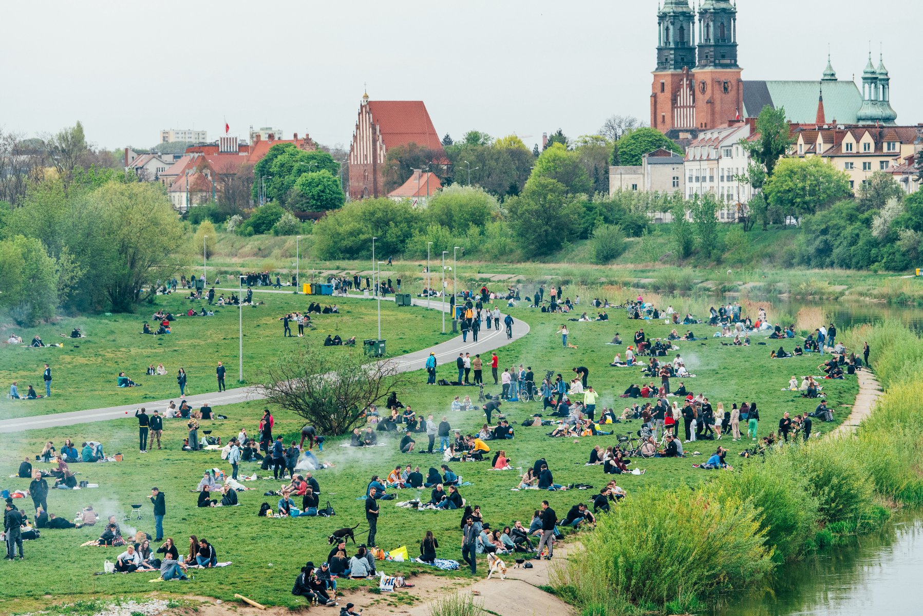 Zdjęcie przedstawia grupę ludzi odpoczywających nad Wartą. W tle katedra. - grafika artykułu