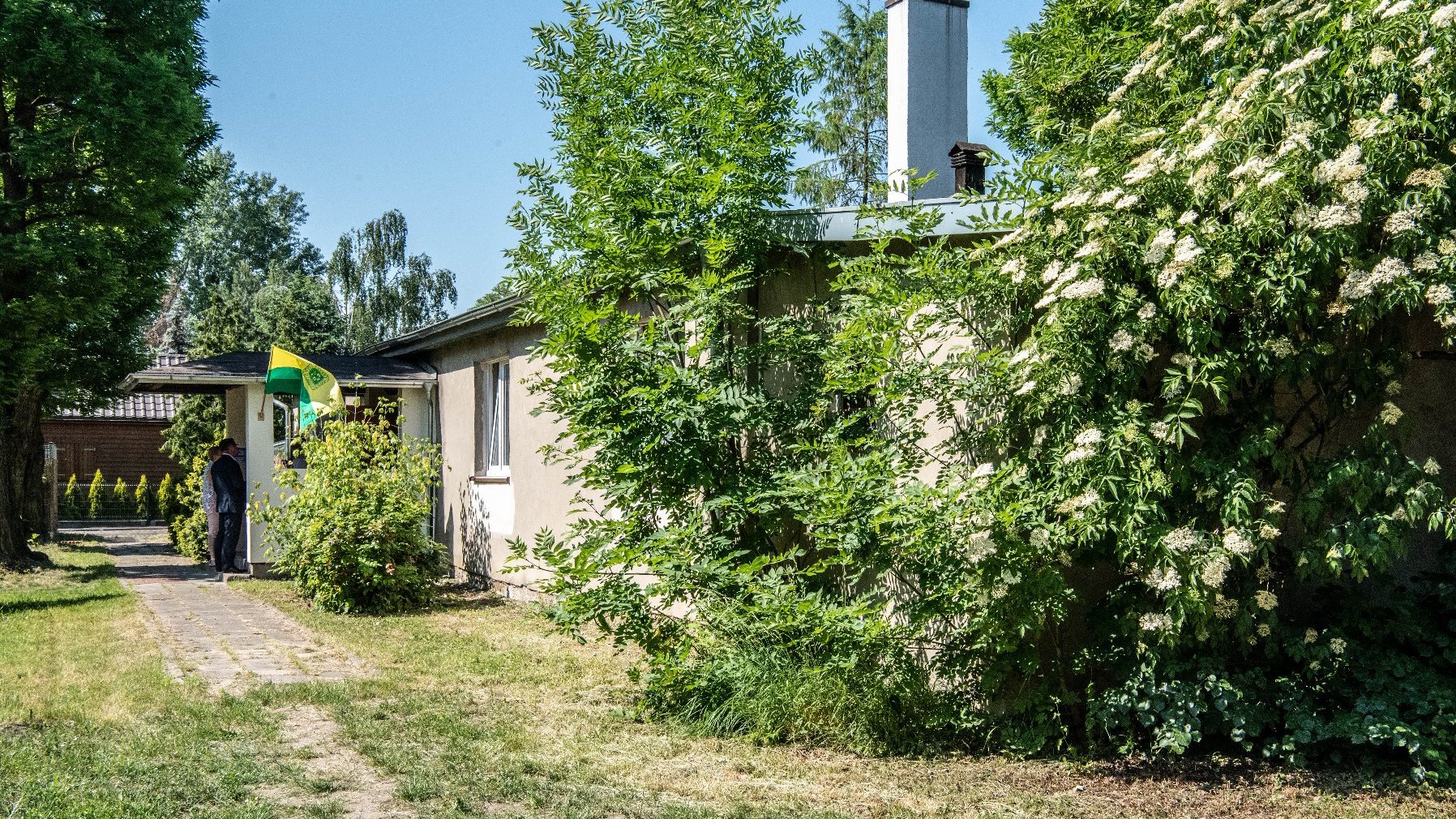 Na zdjęciu świetlica na ogródkach działkowych pośrdód drzew i krzewów