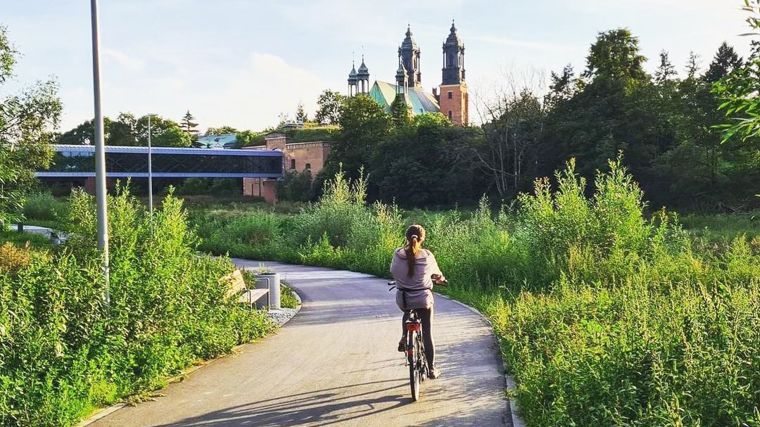 Zdjęcie rowerzystki jadące Wartostradą koło Bramy Poznania