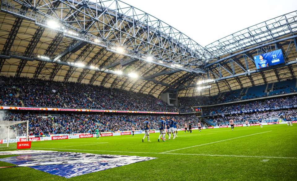 Zdjęcie przedstawia stadion Lecha. Na pierwszym planie widać piłkarzy na murawie w tle trybuny. - grafika artykułu