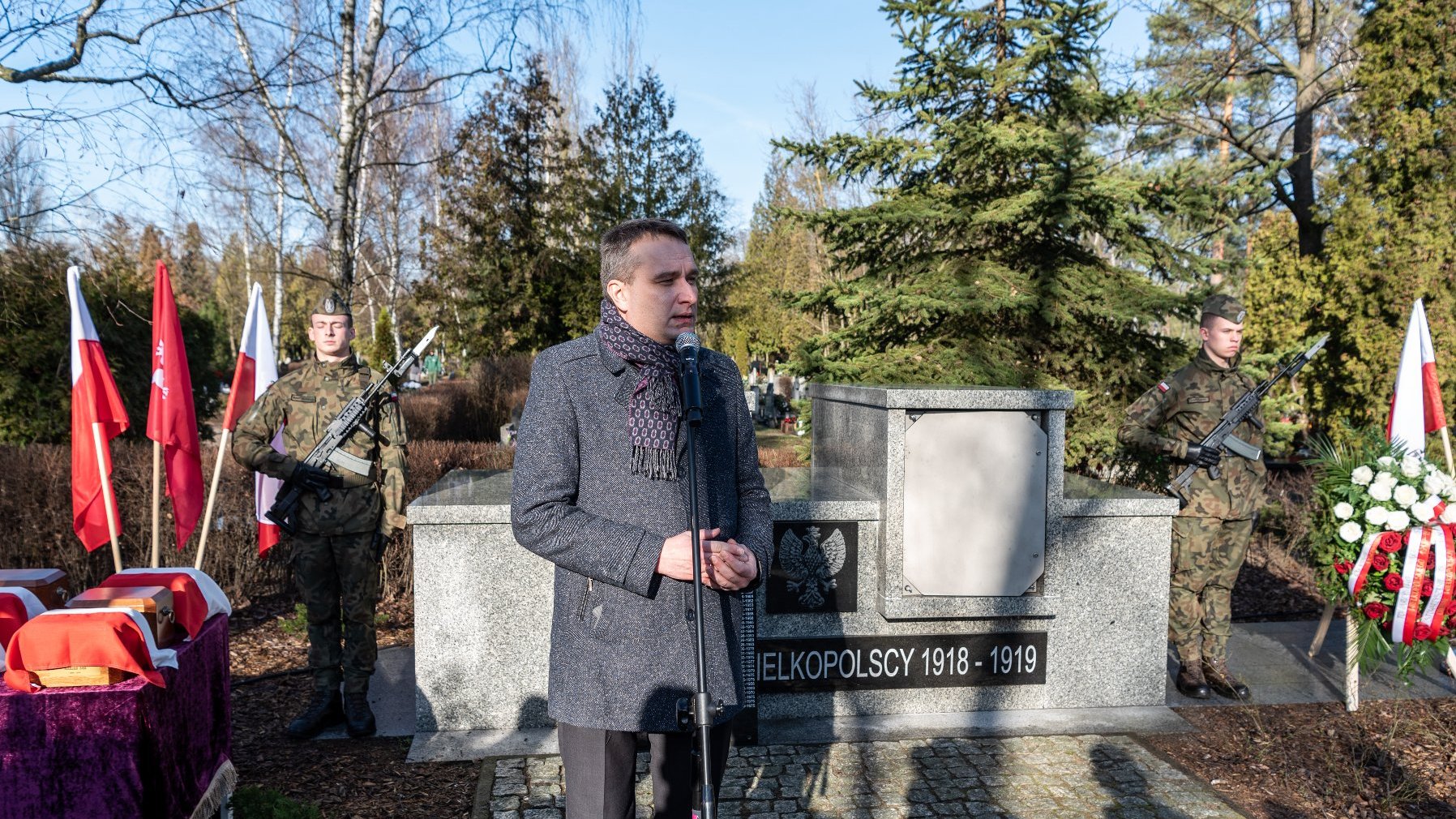 Na zdjeciu zastępca prezydenta Poznania na cmentarzu, przy mikrofonie, obok urn Powstańców, w asyście zołnierzy