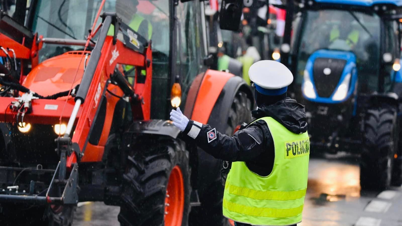 Zdjęcie przedstawia ciągniki i policjanta kierującego ruchem.