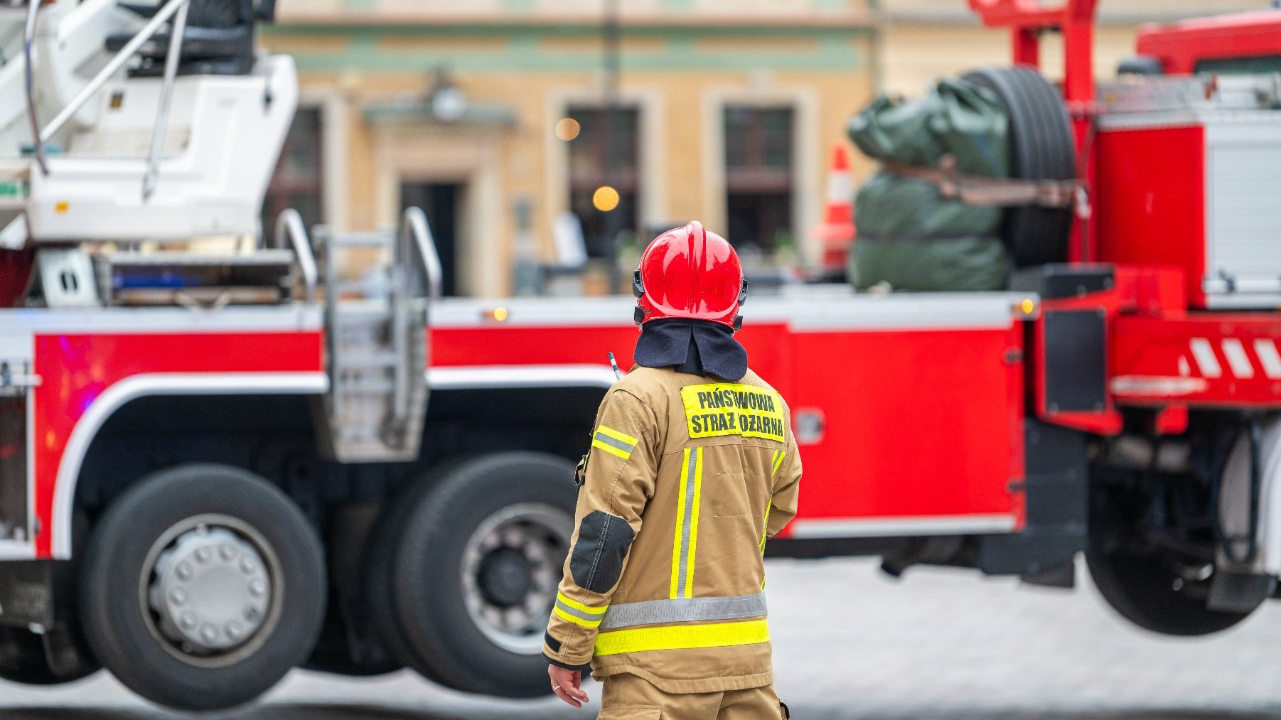 Na zdjęciu strażak stojący tyłem, patrzący na wóz strażacki