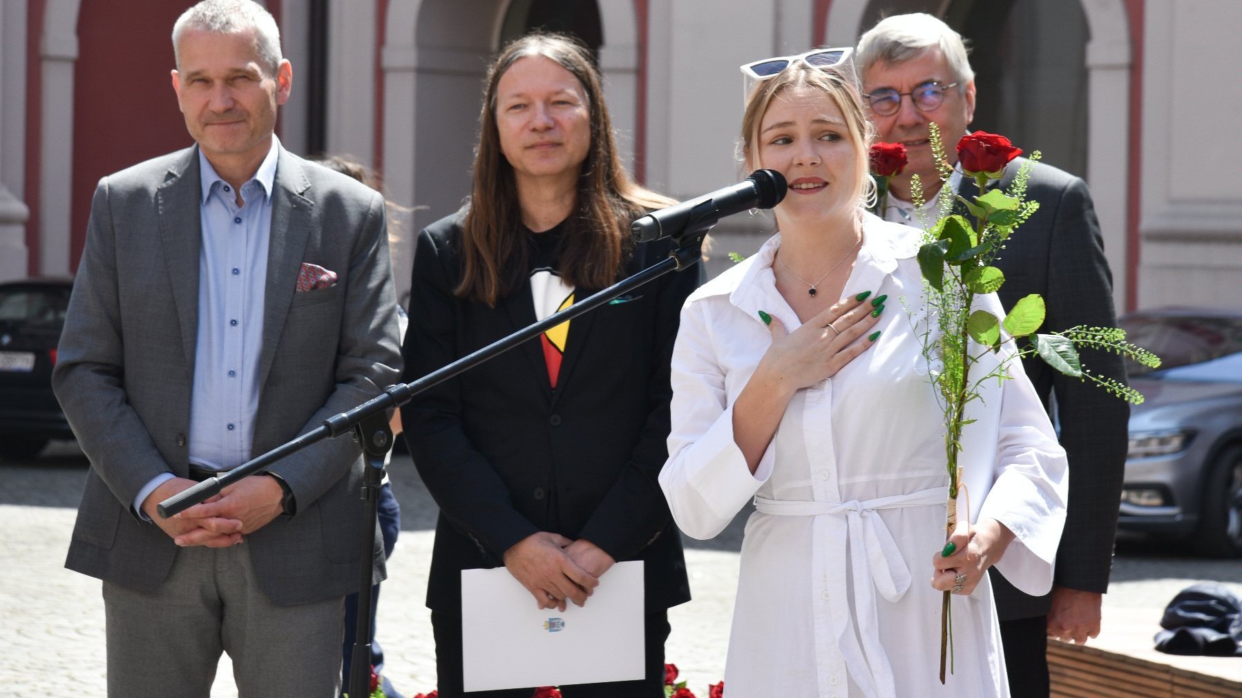 Na zdjęciu młoda kobieta z różą przy mikrofonie, za nią trzech mężczyzn