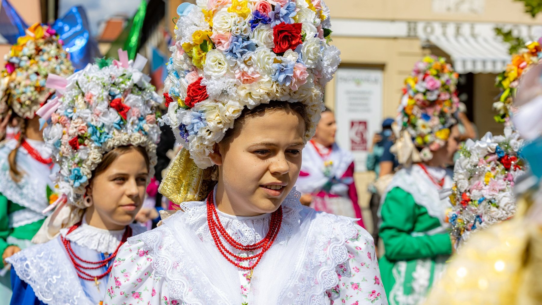 Zdjęcie przedstawia kobiety w strojach bamberki z barwnym kapeluszem z kwiatów i kolorowych sukniach.