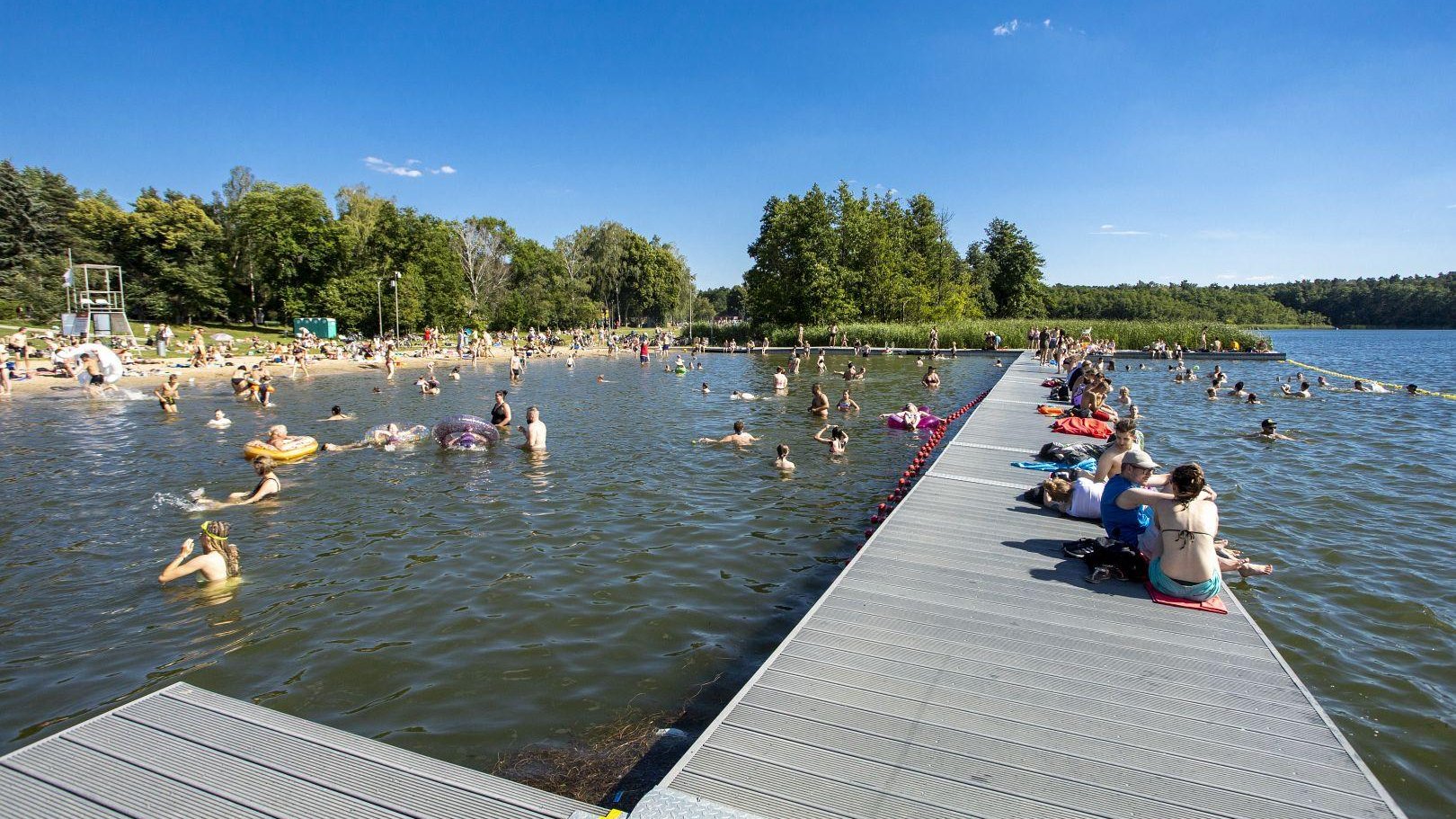 Zdjęcie przedstawia ludzi w wodzie, na pomoście i na plaży. - grafika artykułu