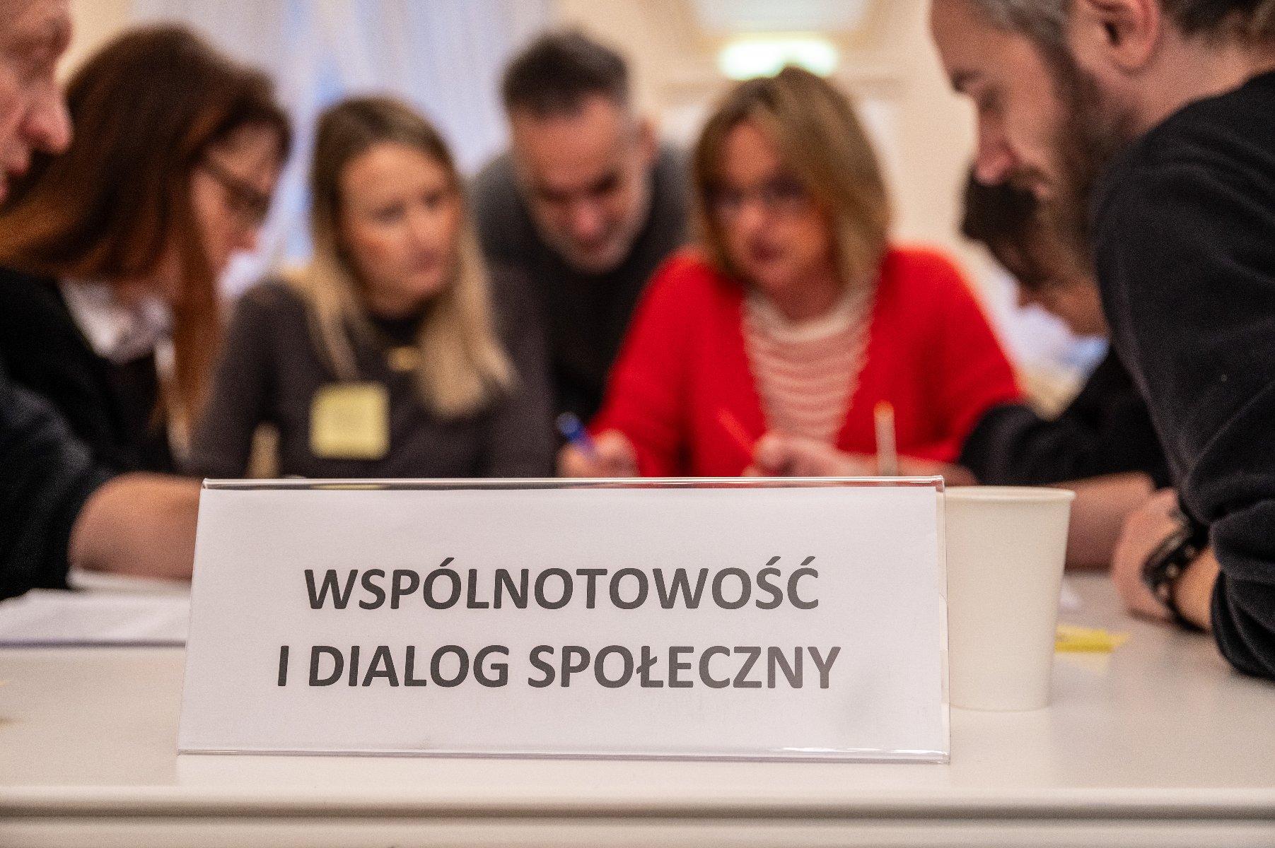 Na zdjęciu kilka dyskutujących osób, na pierwszym planie tabliczka z napisem: wspólnotowość i dialog społeczny - grafika artykułu