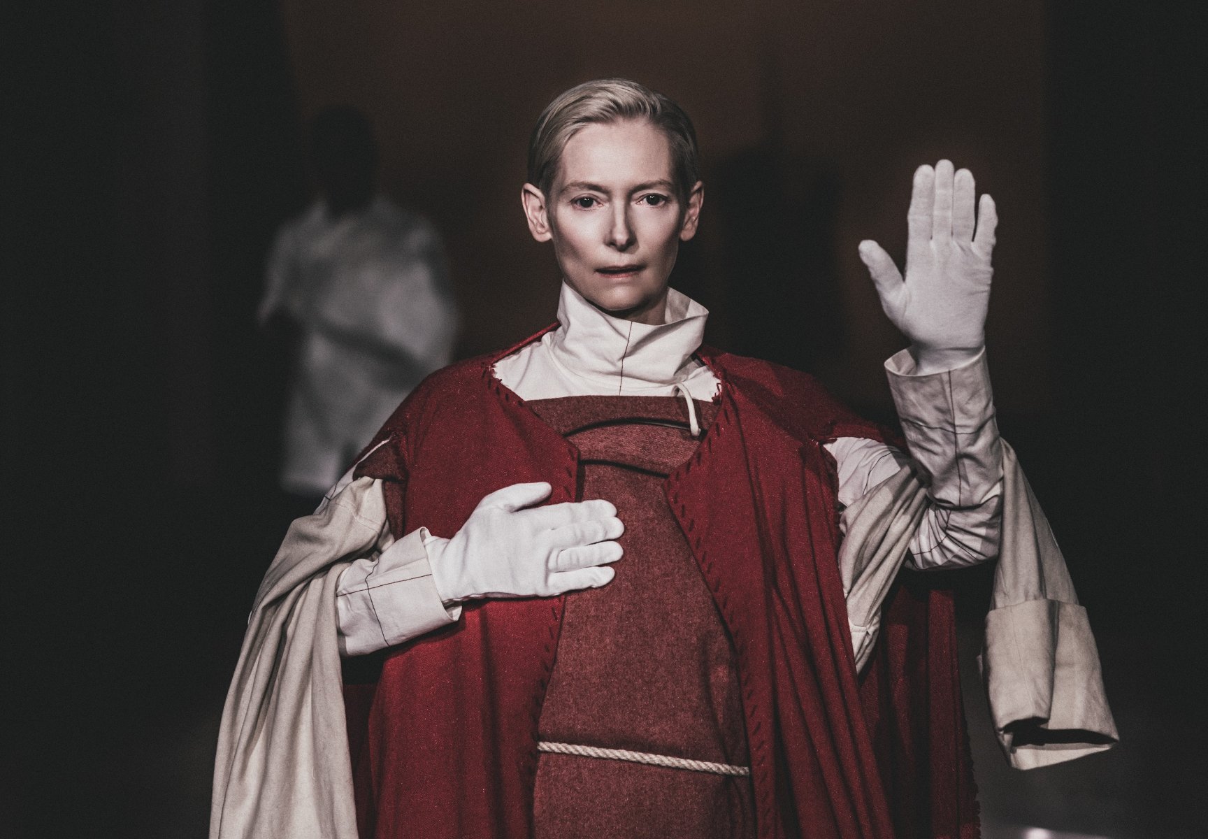 Na zdjęciu Tilda Swinton z jedną dłonią uniesioną w górze - grafika artykułu