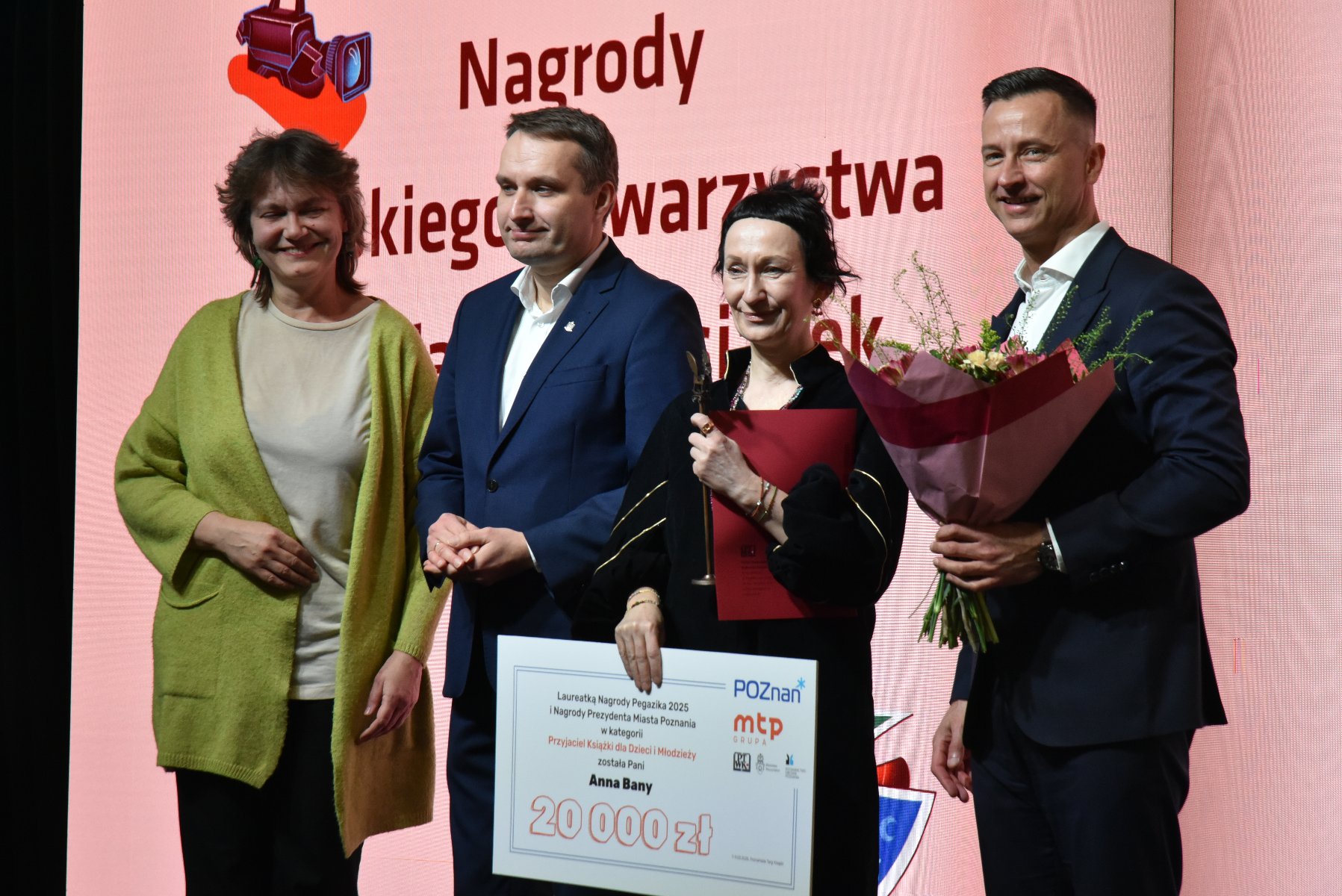 Na zdjęciu cztery osoby, kobieta trzyma statuetkę i duży czek, mężczyzna obok niej trzyma bukiet kwiatów - grafika artykułu