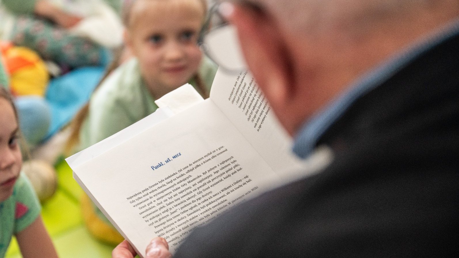 Na zdjęciu mężczyzna czytający dzieciom ksiązkę