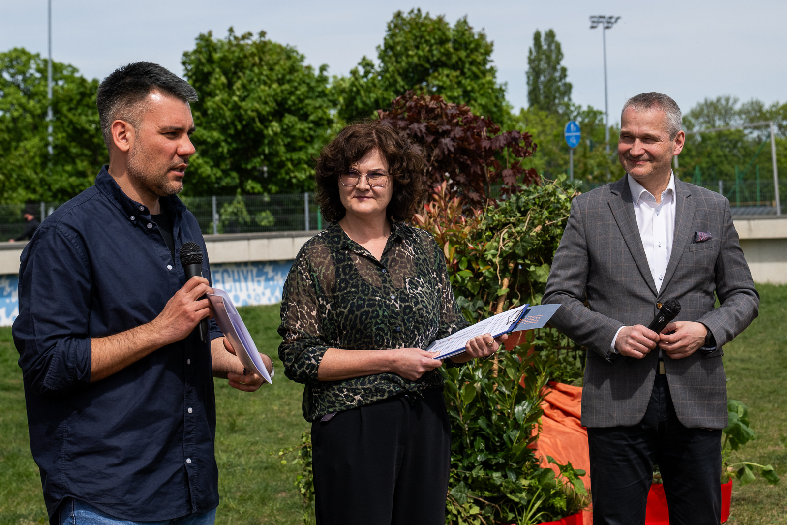 Zdjęcie przedstawiadwóch mężczyzn i kobietę na tle zieleni. Trzymają oni kartki papieru i mikrofony. - grafika artykułu
