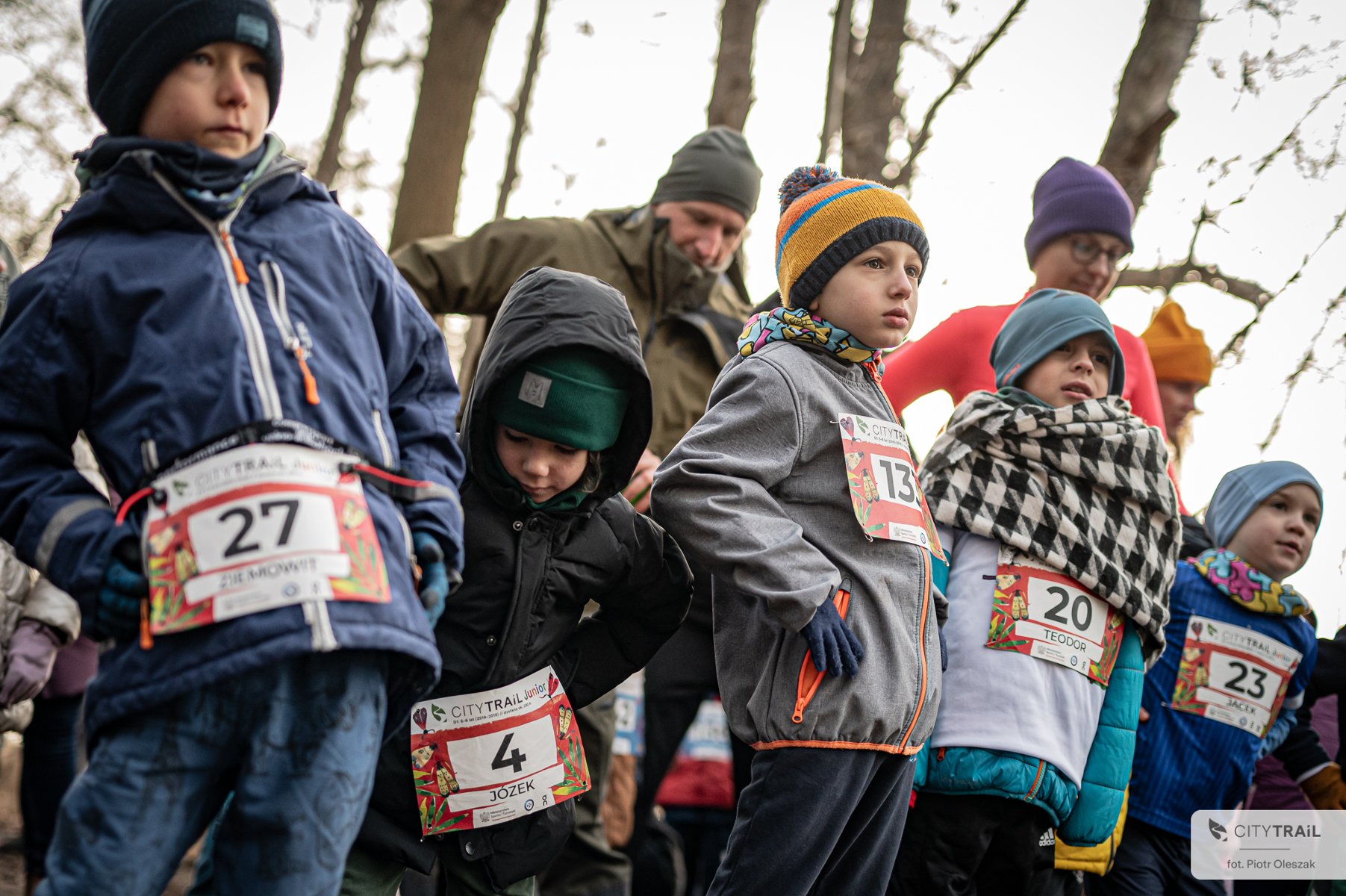 Bieg City Trail w Poznaniu, fot. Piotr Oleszak - dzieci w zimowych strojach, w czapkach i rękawiczach, z zawieszonymi numerami startowymi rozgrzewają się przed biegiem w lesie - grafika artykułu