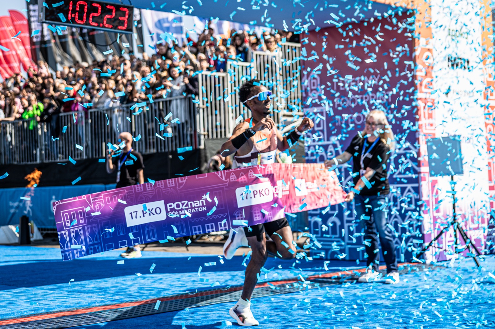 Zwycięzca 17.PKO Poznań Półmaratonu na mecie, fot. Klaudia Berda - mężczyzna w okularach przeciwsłonecznych wbiega na metę wśród konfetti. W tle widać trybunę z kibicami. Zawodnik wbiega po niebieskim dywanie. - grafika artykułu