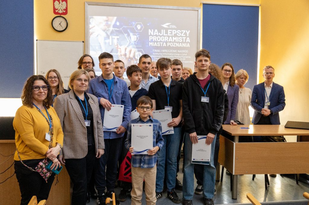 Grupa uczniów w różnym wieku w sali lekcyjnej. Pozują z dyplomami i medalami, uśmiechnięci. - grafika artykułu