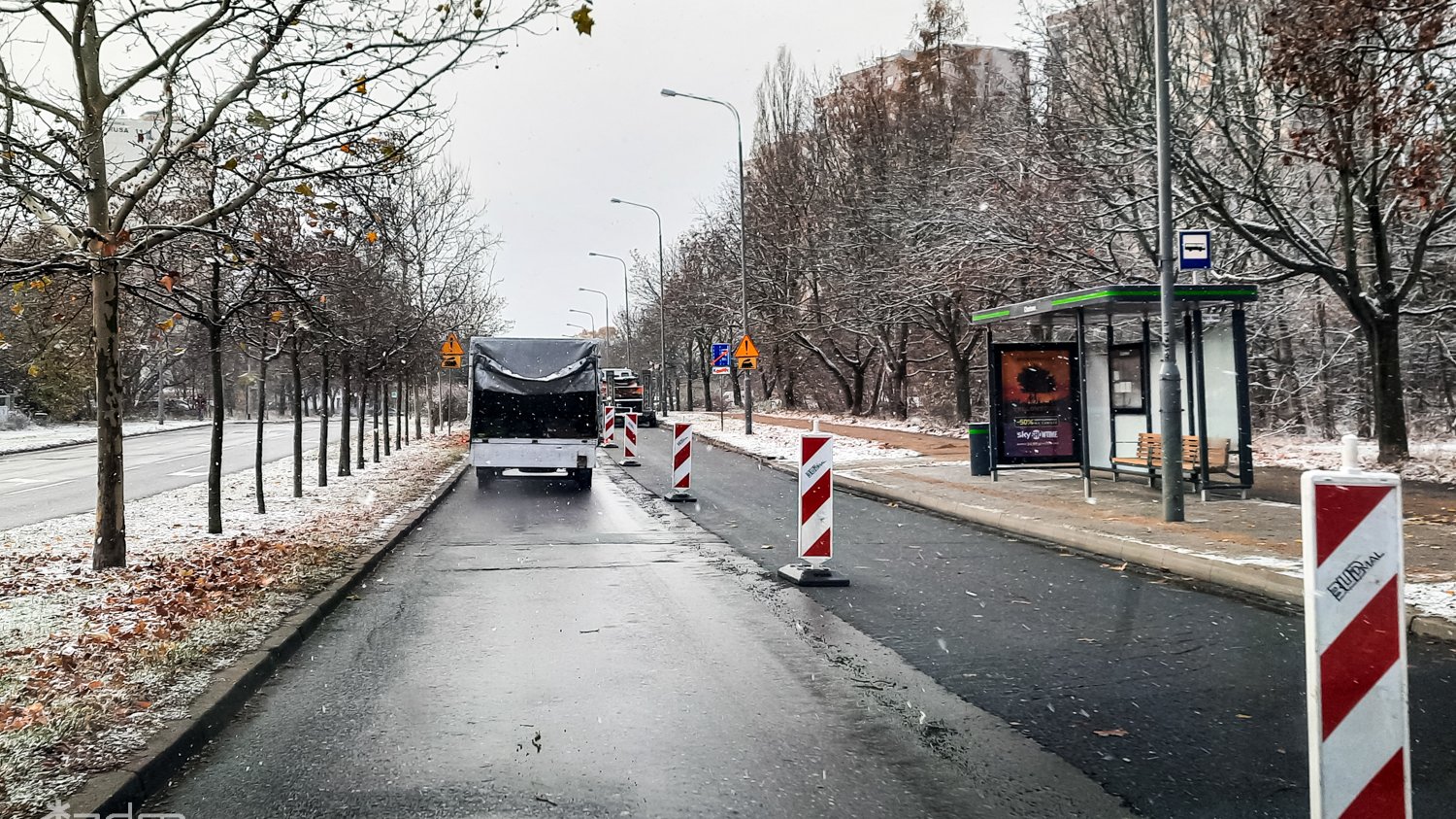 Zeszłoroczne prace na ul. Chartowo na wysokości przystanku autobusowego. Pojedyncze biało--czerwone pylony rozdzielają pasy ruchu. Na trawnikach niewielki śnieg.