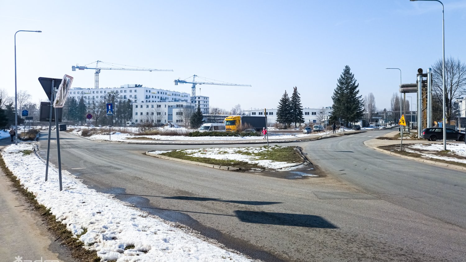 Zdjęcie skrzyżowania, które zmieni się w rondo. Na poboczu snieg, w tle budowa nowych domów mieszkalnych.