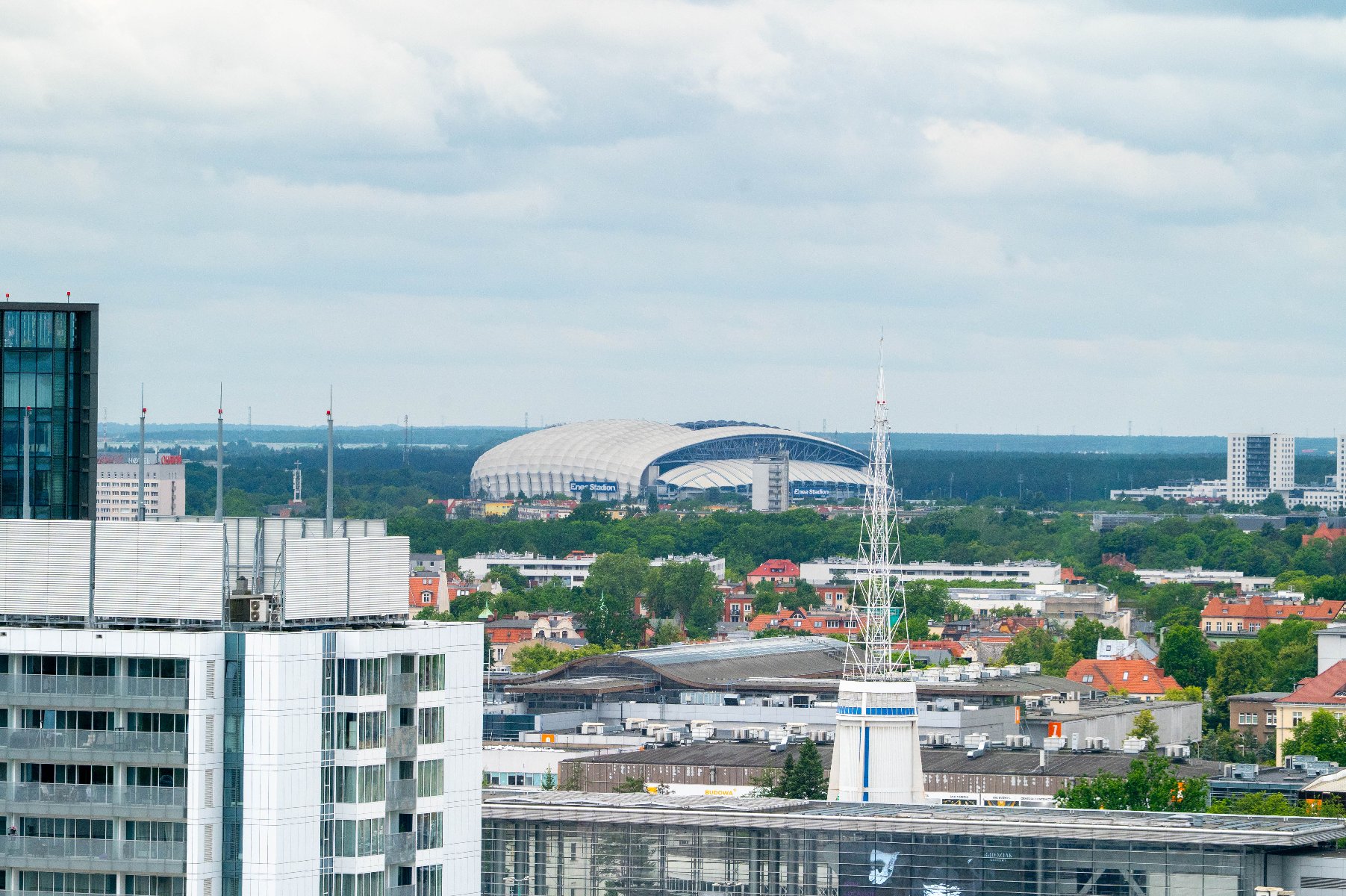 W czwartek, 21 sierpnia o godz. 20:30 na Enea Stadionie Lech Poznań zmierzy się w eliminacjach do Ligi Europy z belgijskim KRC Genk Panorama Poznania z widokiem na Stadion Miejski na horyzoncie. Na pierwszym planie widać nowoczesne budynki mieszkalne i biurowe. Wokół stadionu widać drzewa i zieleń, a w tle rozciąga się las.