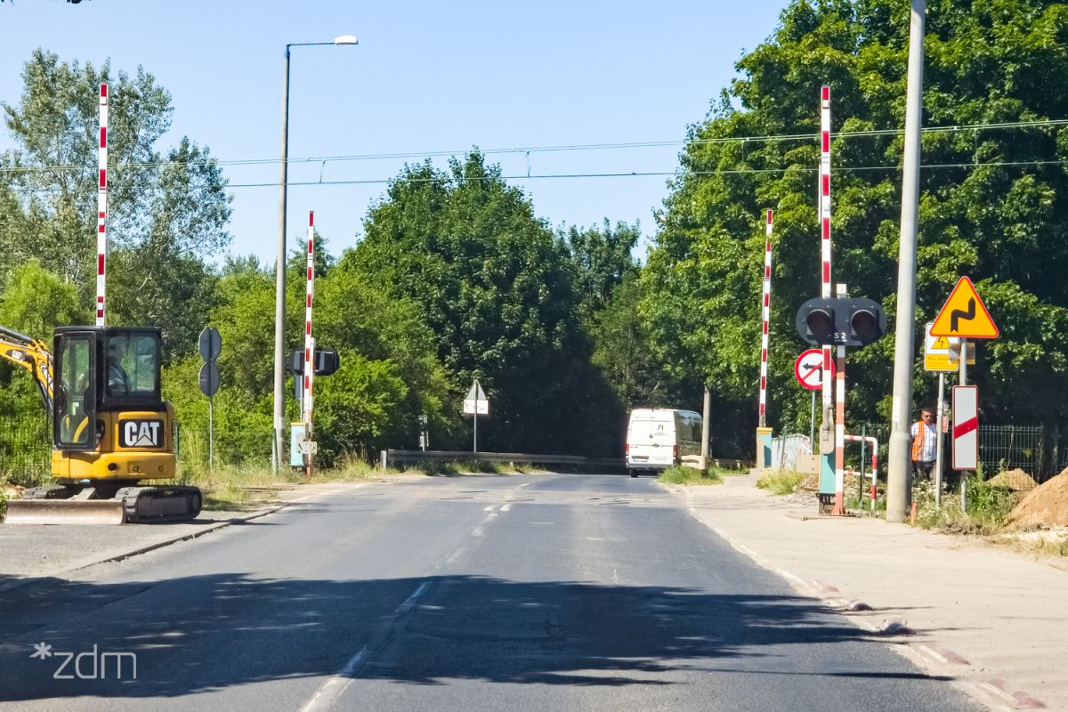 Przejazd na ul. Naramowickiej Przejazd kolejowy z otwartymi szlabanami w ciągu ul. Naramowickiej. Wzdłuż jezdni bariery ochronne i lampy. Na środku jezdni podwójna linia ciągła.