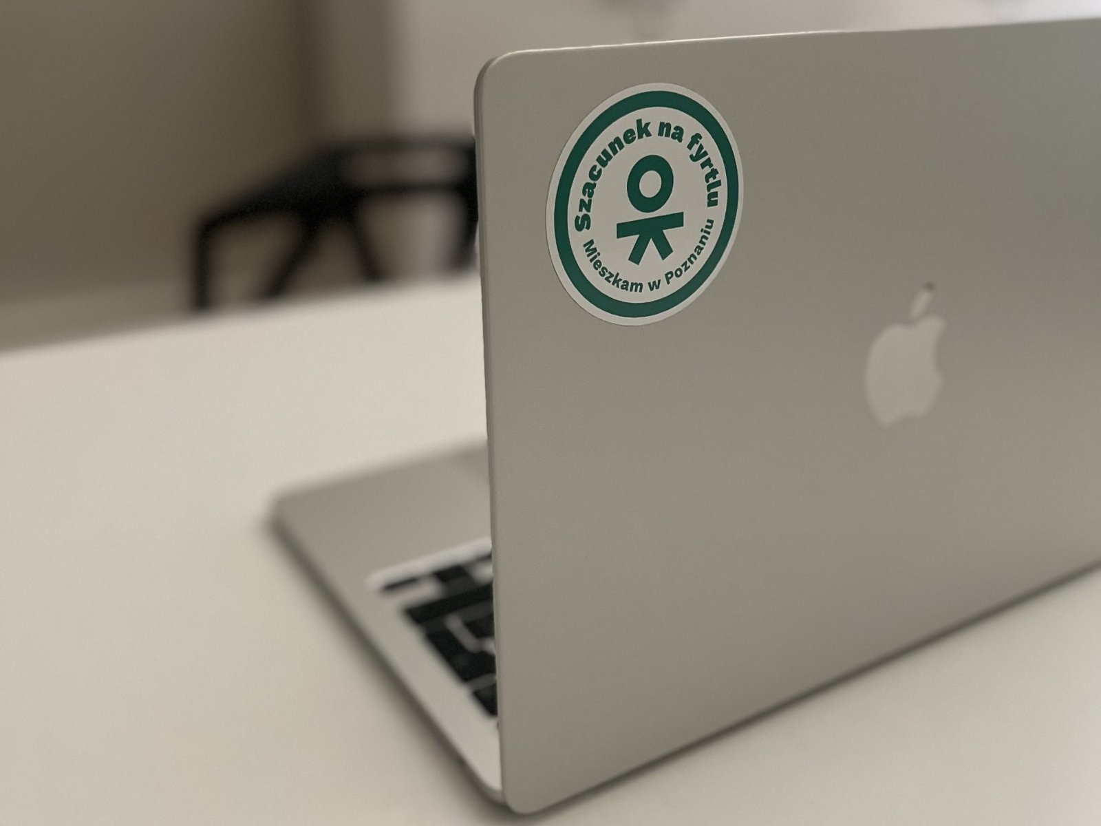 Naklejkę możesz przykleić np na laptop czy zeszyt - gdziekolwiek chcesz. To prosty sposób, by z uśmiechem pokazać, że Poznań to Twoje miejsce. Srebrny laptop, na którym przyklejono naklejkę Szacunek na fyrtlu. Mieszkam w Poznaniu.