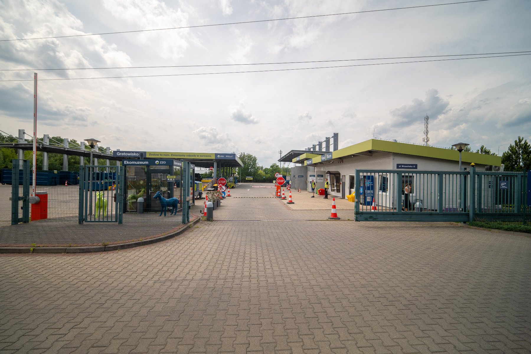 Osoby, które chcą dowiedzieć się czegoś więcej na temat poznańskich Gratowisk oraz zajrzeć na jedno z nich bez wychodzenia z domu, mogą wziąć udział w wirtualnym spacerze/ fot. ZZO Zdjęcie przedstawia gratowisko. Widać na nim plac i kontenery, pod które można podjechać samochodem, a także szyld z napisem gratowisko i adresem strony internetowej ZZO.