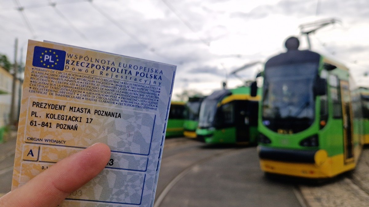 Ręka trzyma dowód rejestracyjny. W tle widać tramwaje