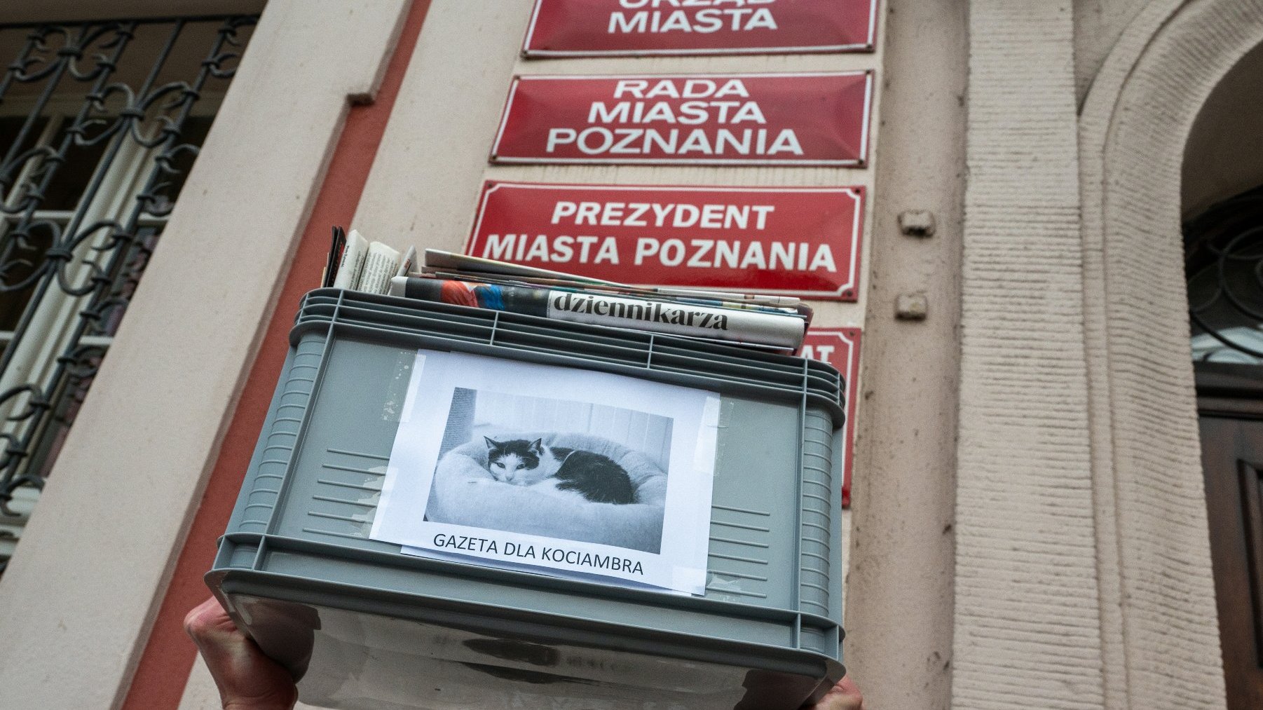 Na zdjęciu skrzynka z gazetami na tle tabliczek z napisami Urząd Miasta, Rada Miasta Poznania i Prezydent Miasta Poznania
