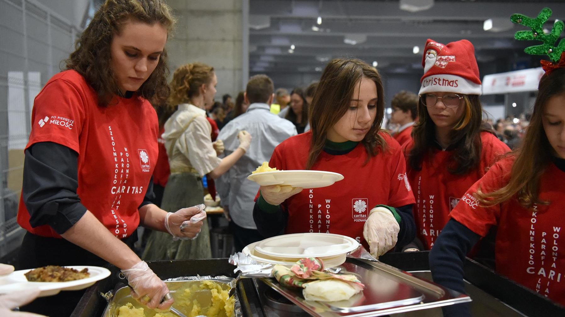Na zdjęciu kobiety w koszulkach Caritas nakładają jedzenie na talerze