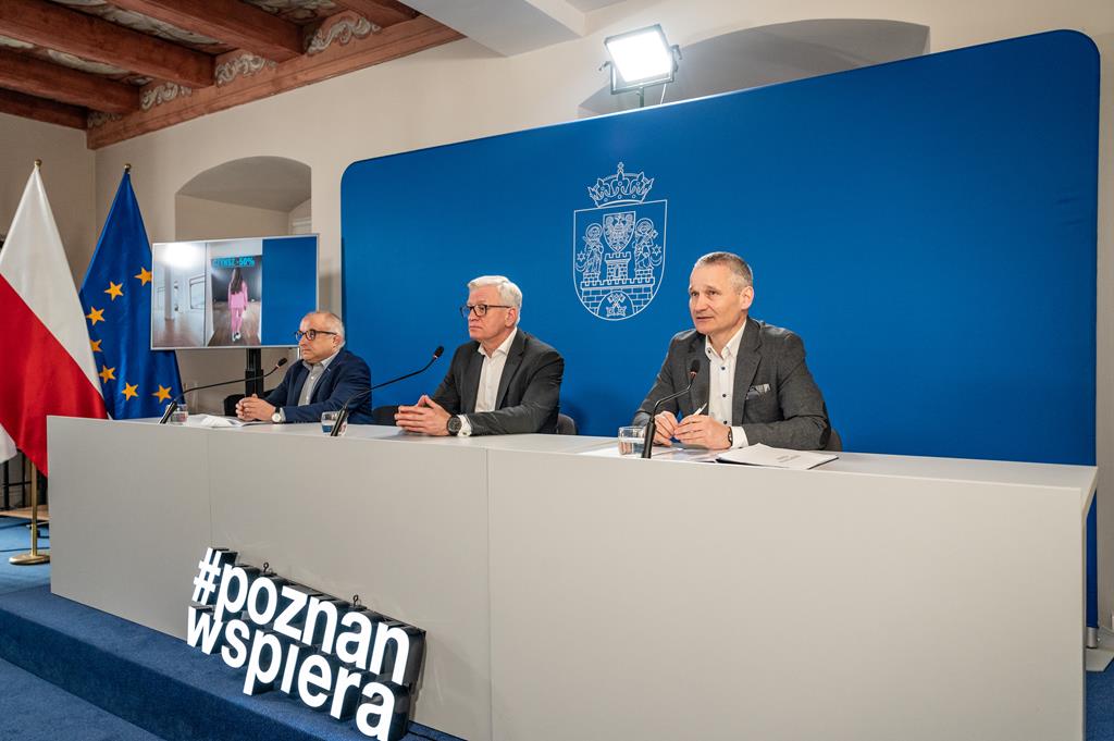 Na zdjęciu trzech mężczyzn za stołem konferencyjnym, w środku prezydent Poznania - grafika artykułu