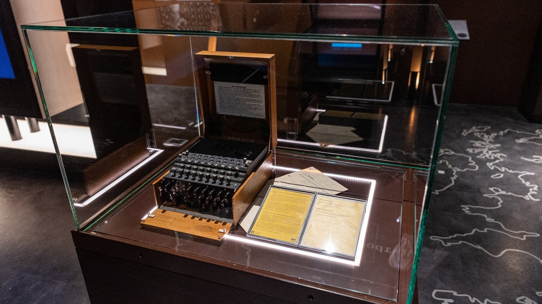 Zdjęcie przedstawia niemiecką maszynę szyfrującą Enigma umieszczoną w gablocie.