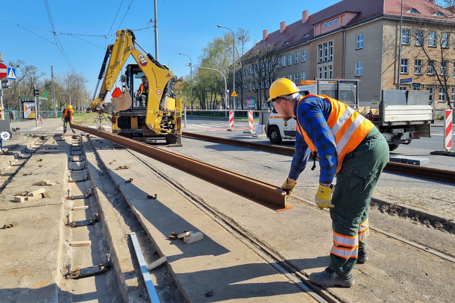 Zdjęcie przedstawia pracowników służb torowych układającyh torowisko. W tle koparka. - grafika artykułu