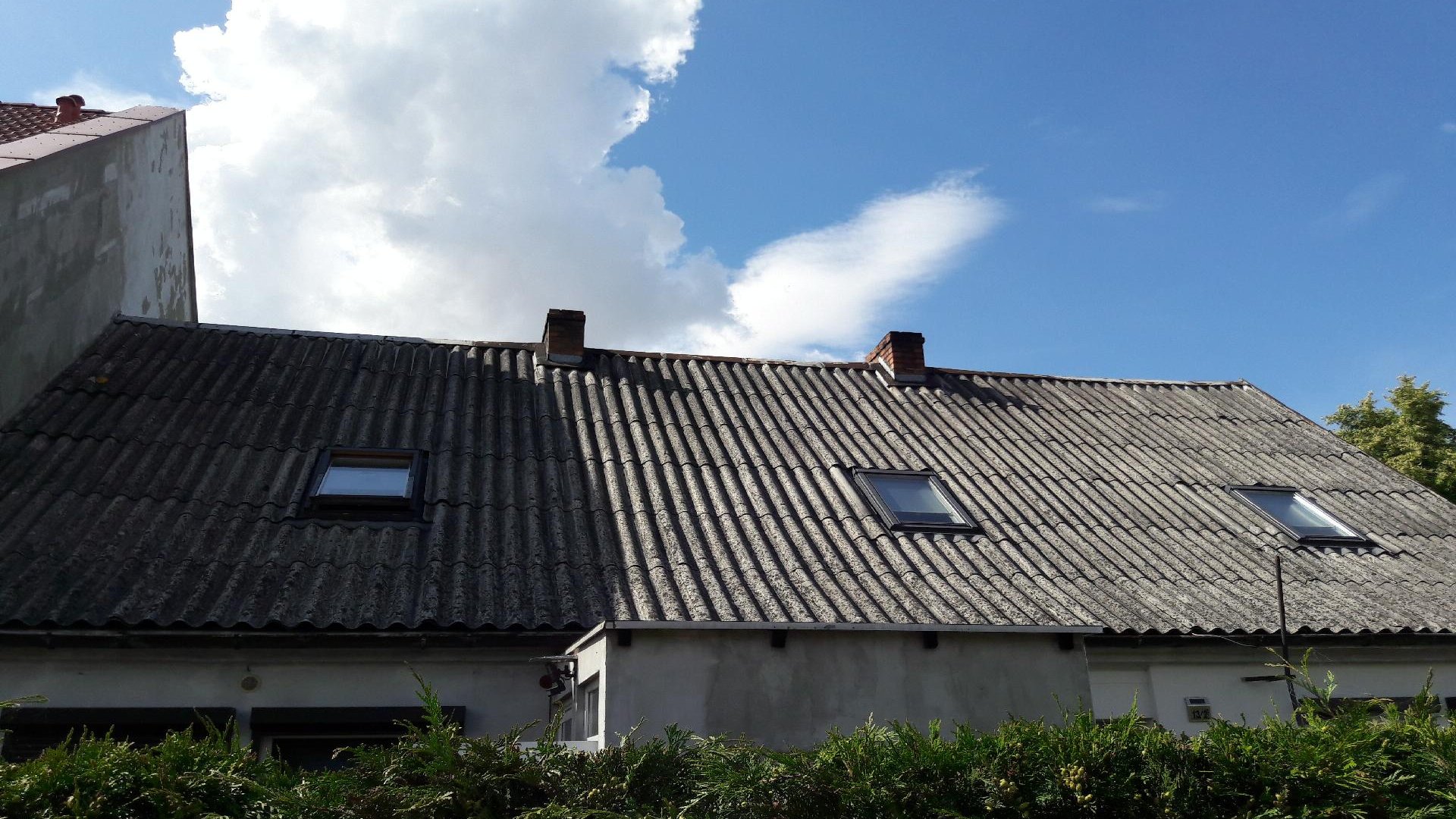 Na zdjęciu dach domu pokryty eternitem, nad nim niebo z chmurami