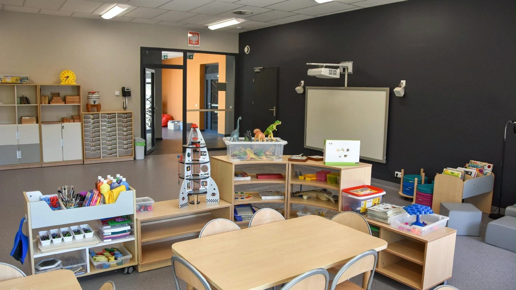 Na zdjęciu sala w przedszkolu z zabawkami, stolikami i edukacyjnymi przedmiotami - grafika artykułu