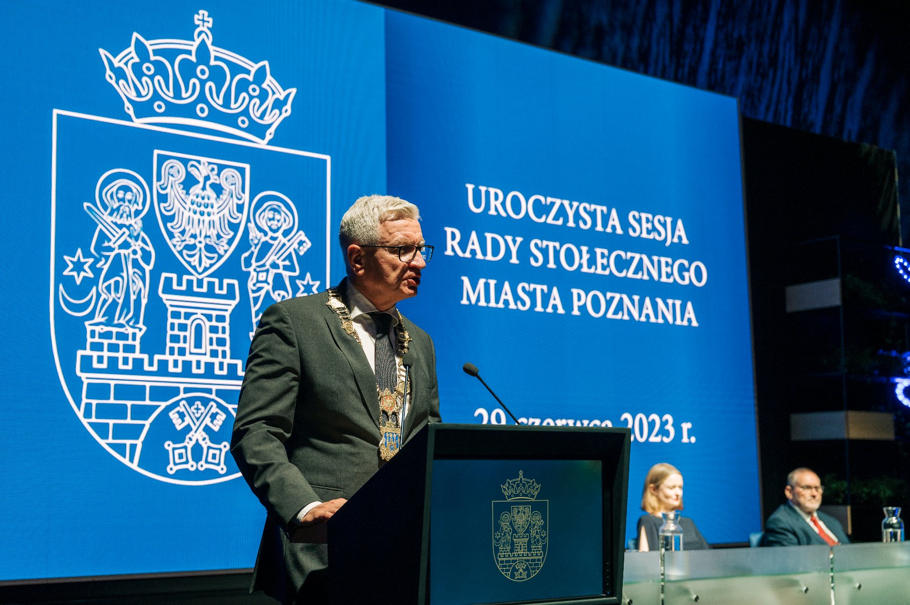 Na zdjeciu prezydent Poznania przy mikrofonie, w tle napis: uroczysta sesja rady stołecznego miasta Poznania - grafika artykułu