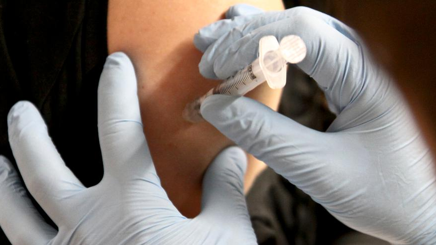Na zdjęciu dłonie podające komuś szczepionkę, w centrum zdjęcia strzykawka - grafika artykułu