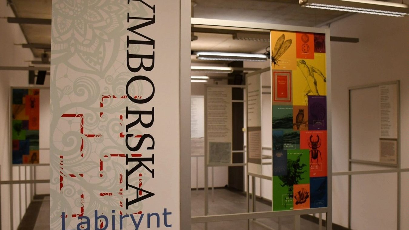 Fotografia przedstawia przestrzeń galerii, w której na planszach prezentowane są wiersze poetki i kolorowe okładki wydań poezji.