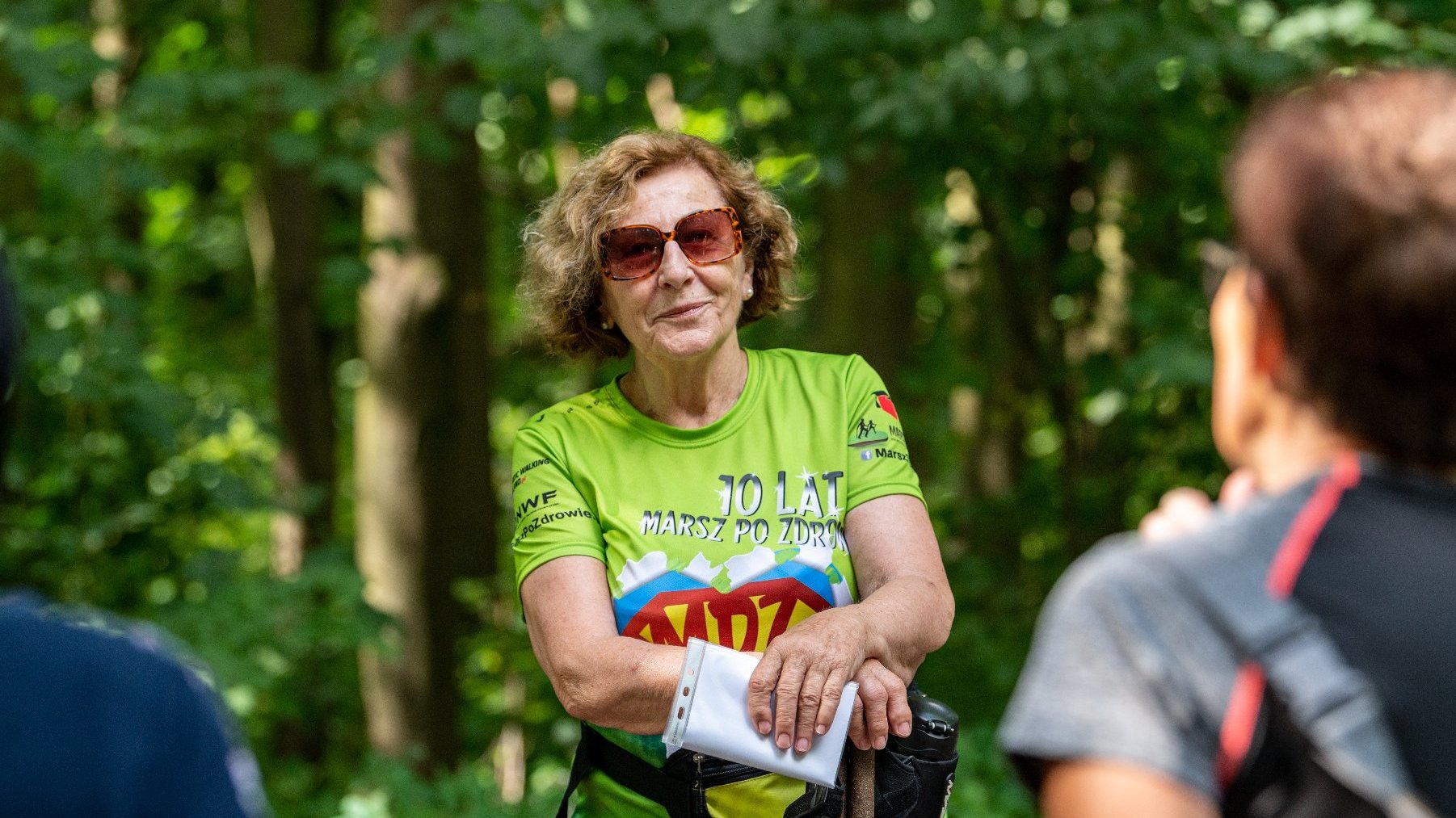 Galeria zdjęć przedstawia grupę seniorów w strojach sportowych z kijkami do nordic walking.