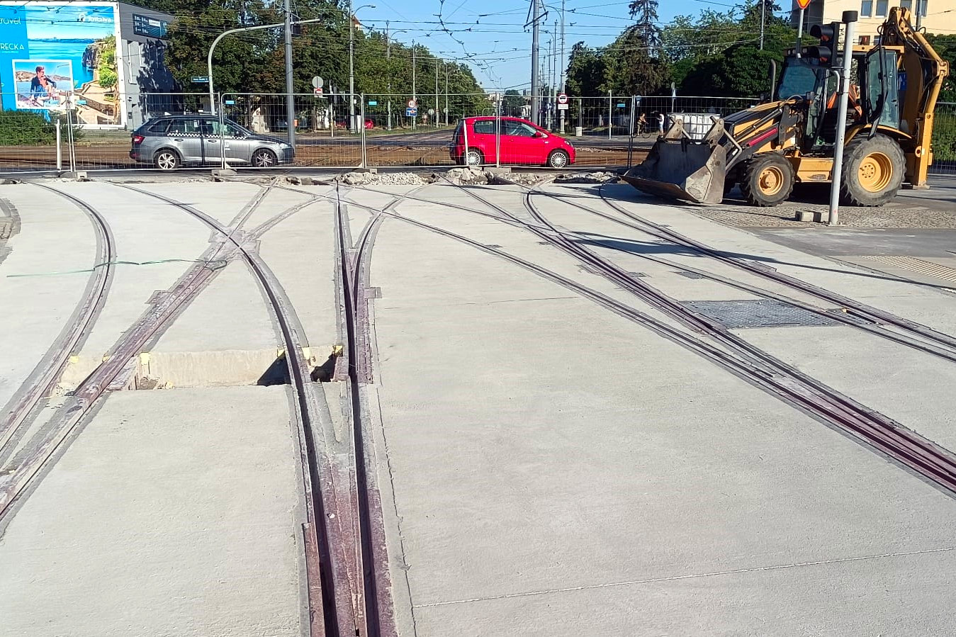 Na zdjęciu zbliżenie na łuki szyn tramwajowych, w tle widać koparkę i samochody - grafika artykułu