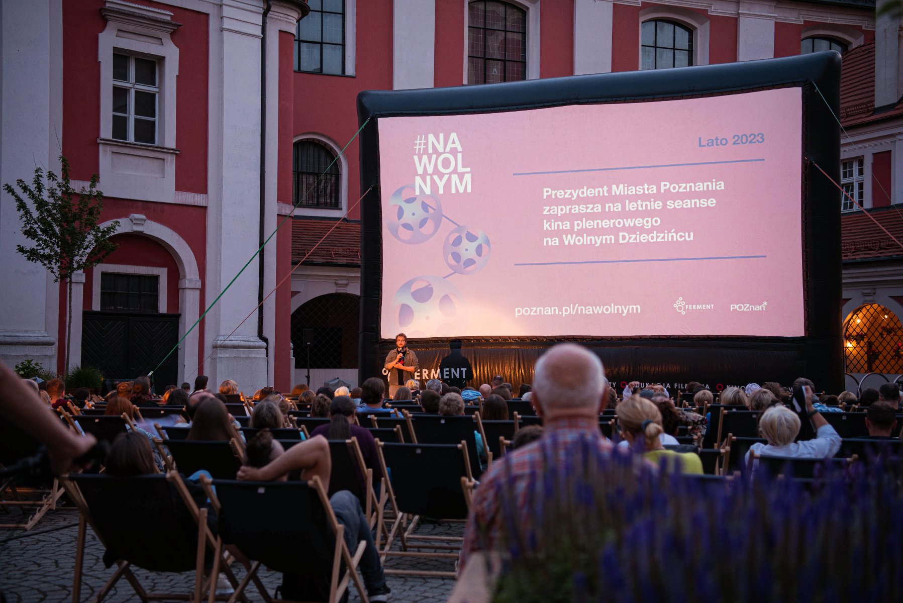 na zdjęciu ludzie zebrani na Wolnym Dziedzińcu oglądają kino plenerowe - grafika artykułu