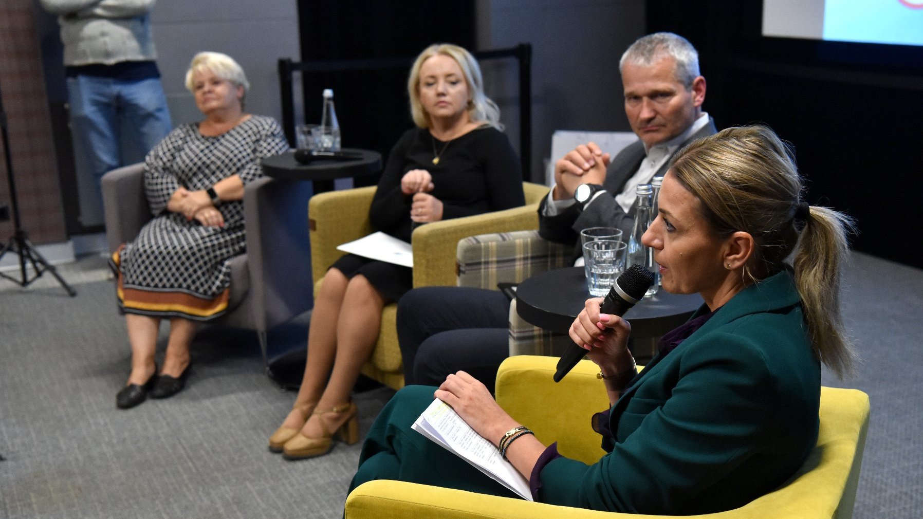 Na zdjęciu konferencja prasowa, cztery osoby na krzesłach, wśród nich trzy kobiety, jedna z nich trzyma mikrofon