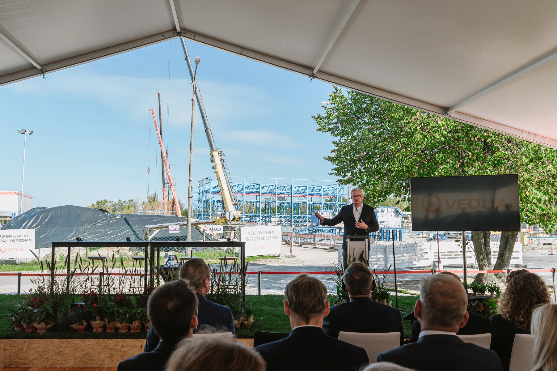Zdjęcie przedstawia Jacka Jaśkowiaka, prezydenta Poznania, stojącego przy mównicy. W tle plac budowy z dzwigami. - grafika artykułu