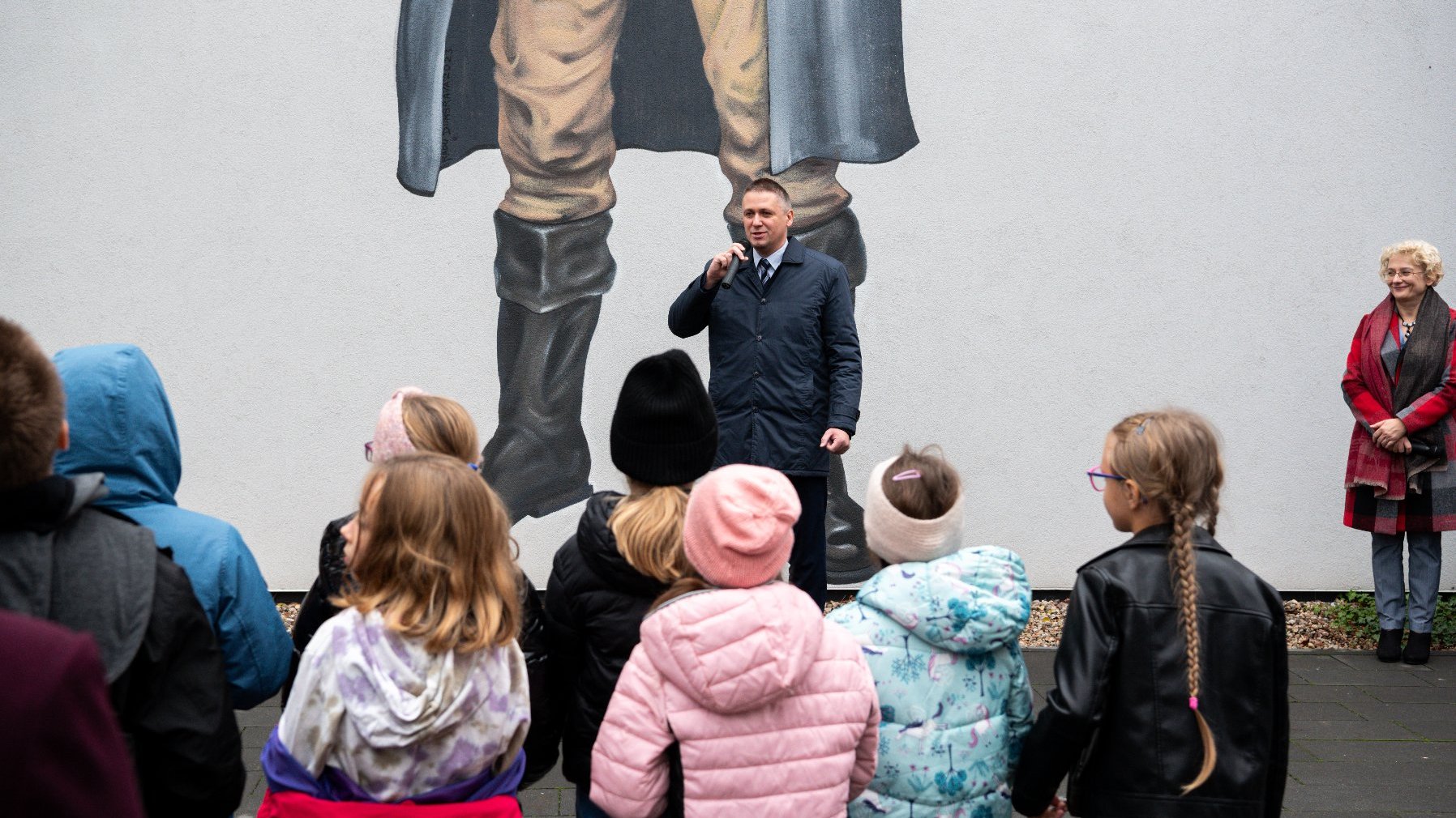 Zdjęcia z odsłonięcia muralu z Pawłem Edmundem Strzeleckim - na muralu mężczyzna z koalą na ramieniu, mężczyzna trzyma w ręku lupę, przez którą patrzy na kulę ziemską. Dookoła zgromadzeni ludzie