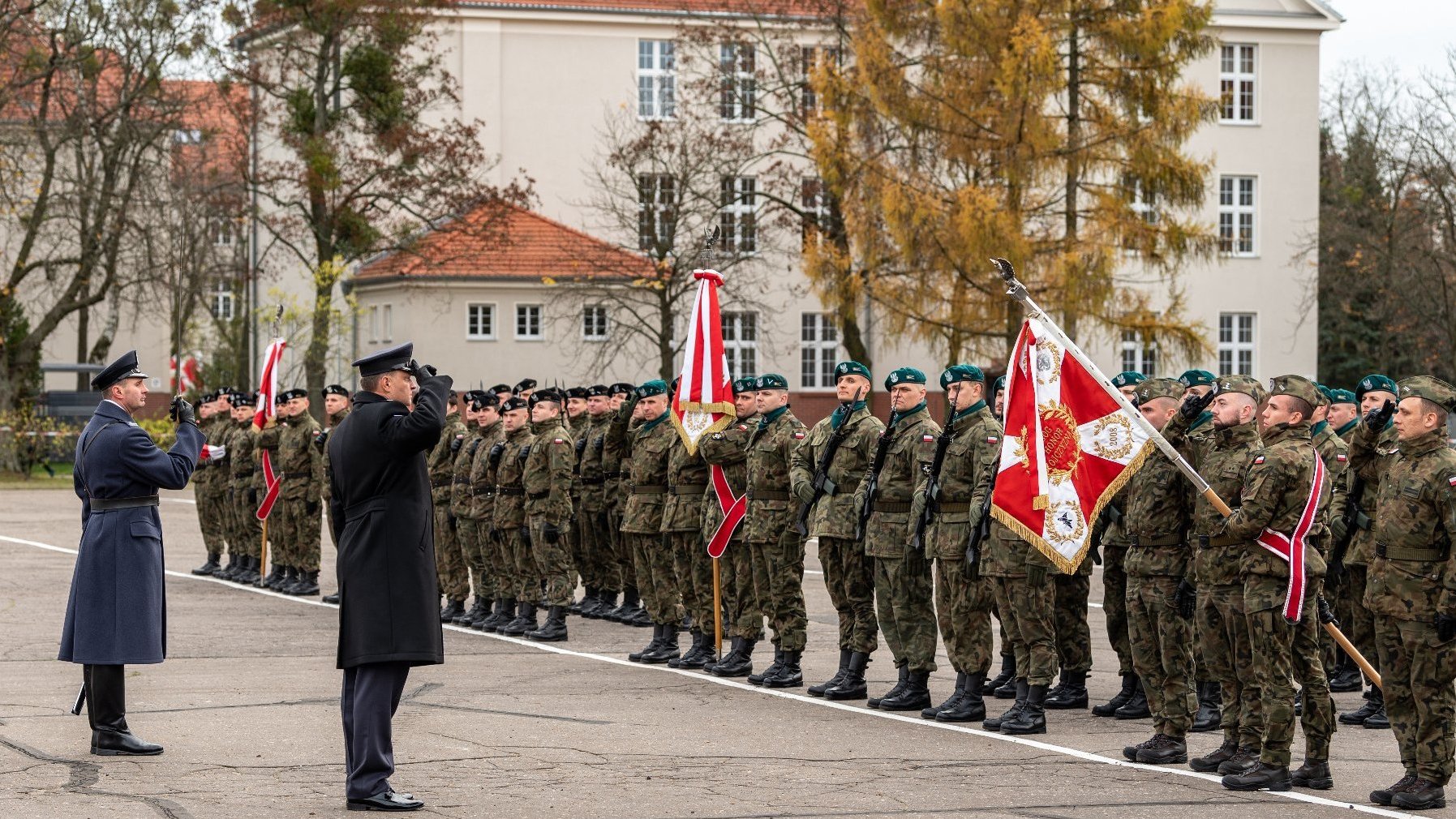Zdjęcie przedstawia poczet sztandarowy Wojska Polskiego oraz salutujących żołnierzy.