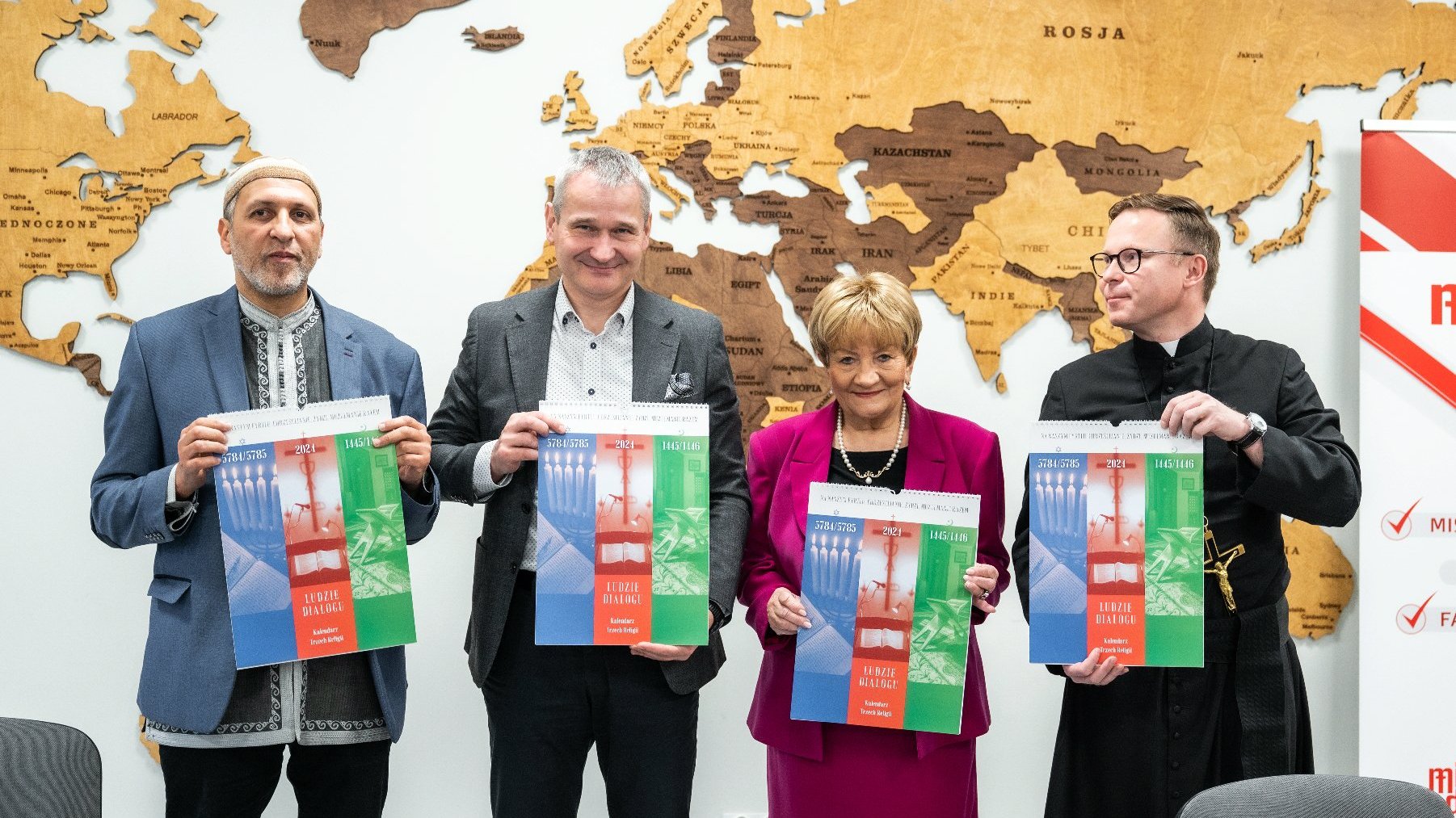 Na zdjęciu trzech mężczyzn i kobieta, każde z nich trzyma kalendarz, w tle mapa świata