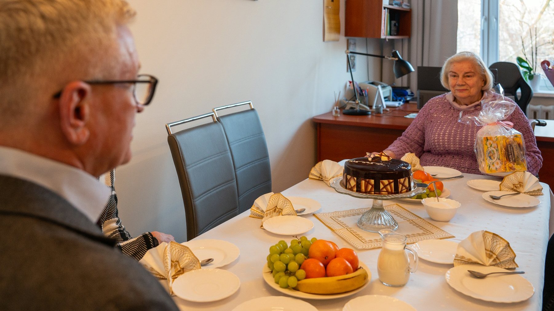 Na zdjęciu prezydent Poznania i była dyrektorka DPS przy stole, na którym stoi urodzinowy tort
