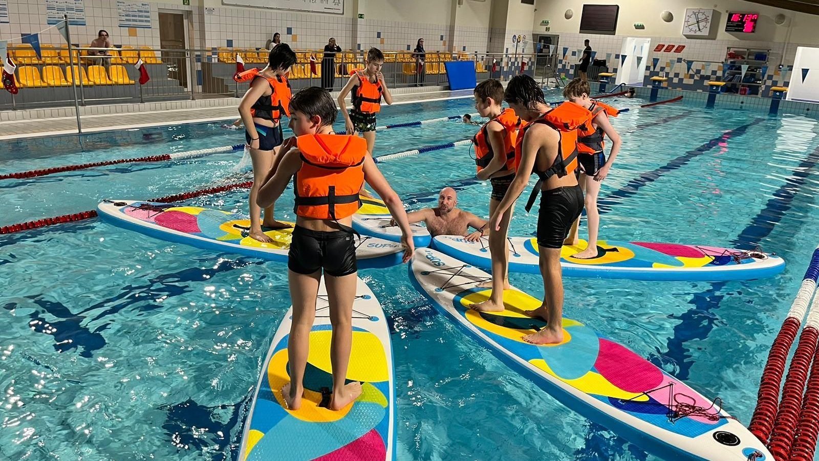 Na zdjeciu grupa dzieci ćwiczących pływanie na deskach