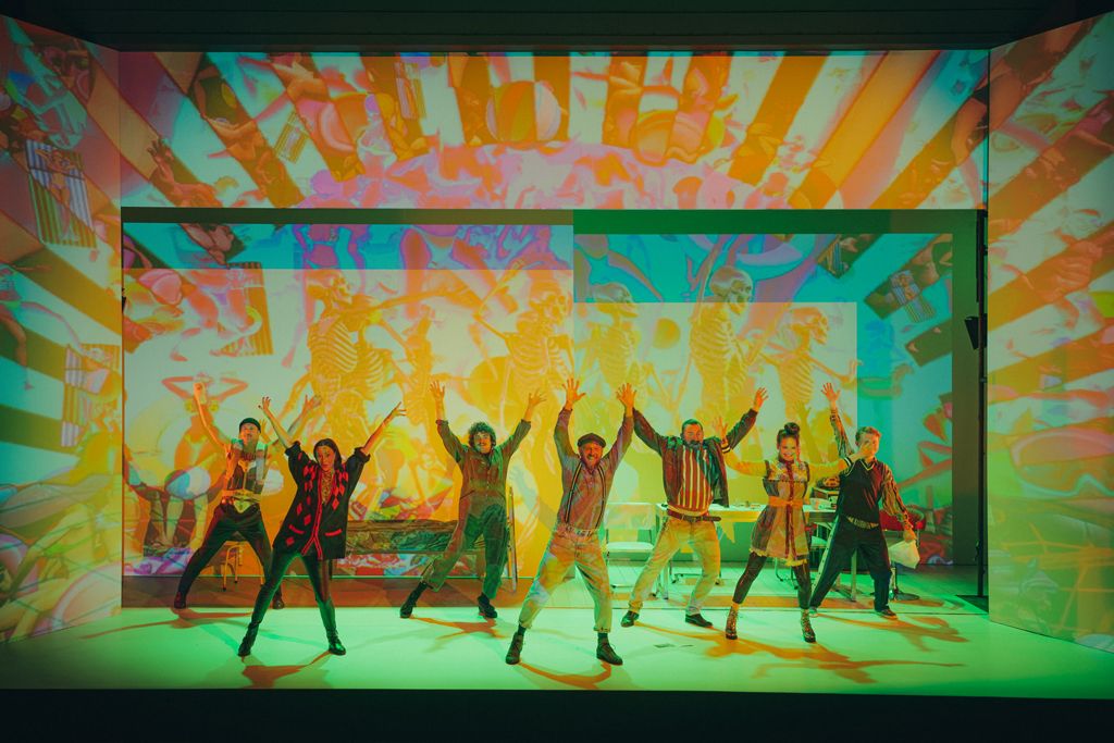 Na zdjęciu kadr ze spektaklu - aktorzy z rękami w górze, na tle kolorowych świateł - grafika artykułu