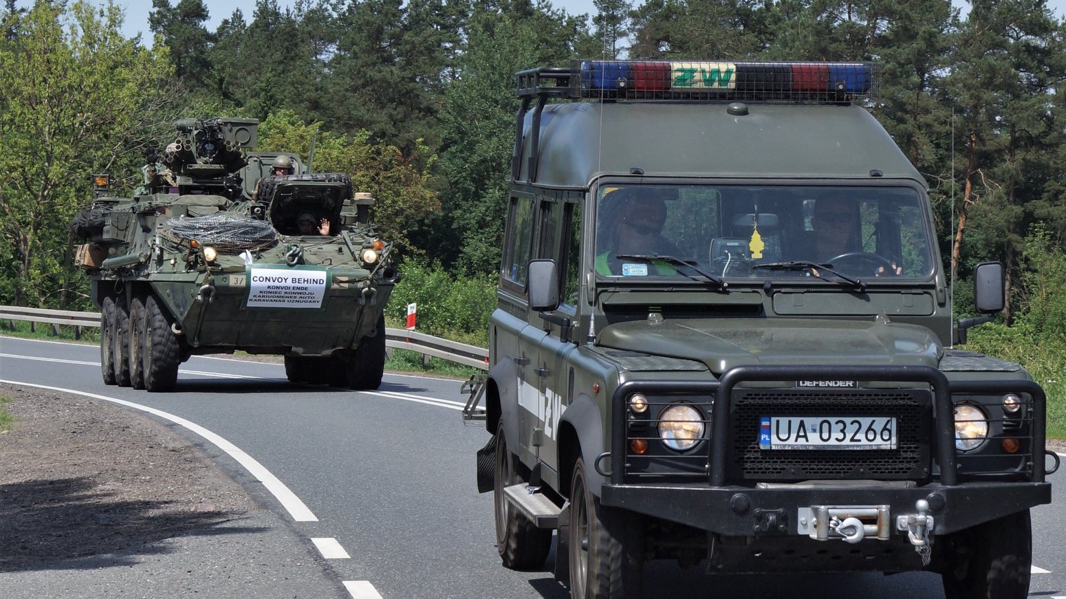 Zdjęcie przedstawia samochody wojskowe na drodze.