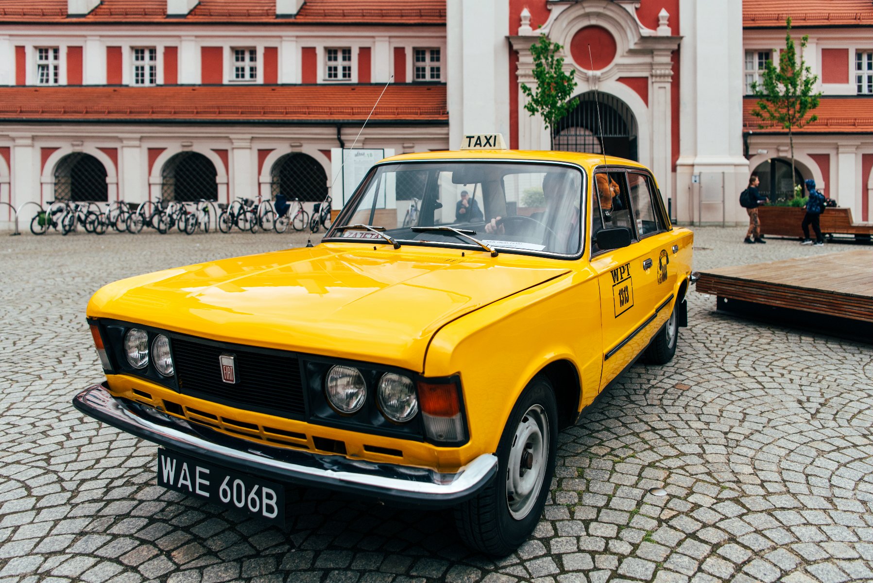 Zdjęcie przedstawia żółtą taksówkę stojącą na dziedzińcu Urzędu Miasta Poznania. - grafika artykułu